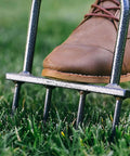 Foot pressing down on Beefy Spike Lawn Aerator Tool With 37 Inch Handle in a grassy lawn, demonstrating use.
