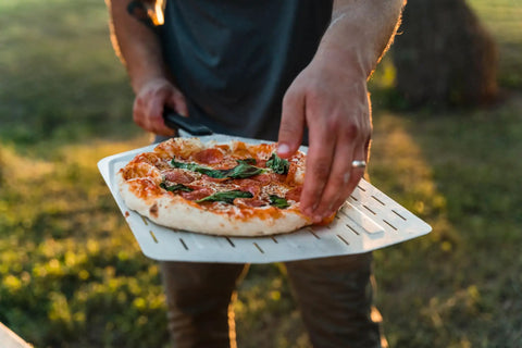 Person using 14 Inch Perforated Pizza Peel With Long Handle Aluminum Lightweight Pizza Paddle For Turning And Lifting Pizza