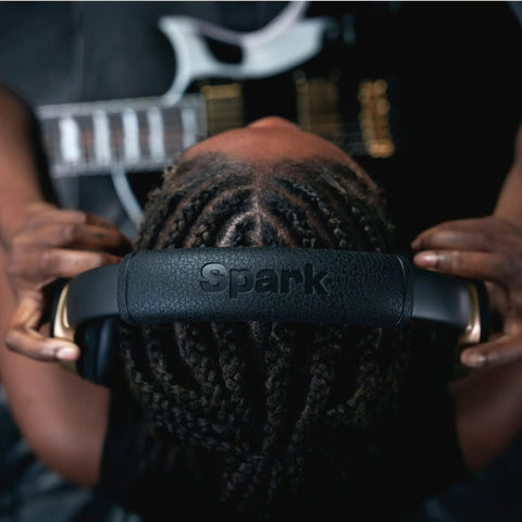 Person wearing Spark NEO Wireless Guitar Headphone Amp And AI Powered Guitar Rig, holding headphones with guitar in background.