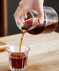 Pouring coffee from a glass jug into a clear cup, showcasing Premium Glass Cold Brew Drip Tower With Adjustable Flow Dripper For Smooth Cold Extraction Coffee Maker 600 Milliliter Gray Body Great For Late Night Study Grinds And Smooth Backyard Sips.