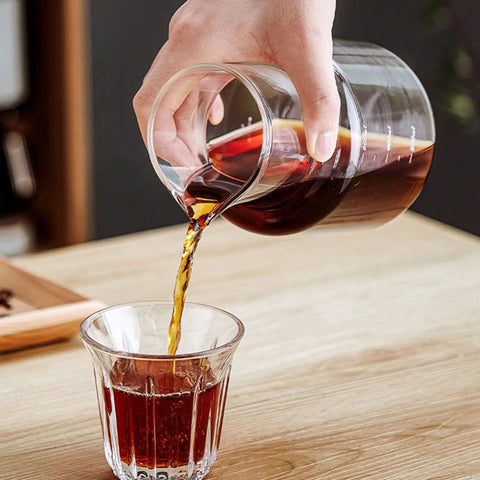 Pouring coffee from a glass jug into a clear cup, showcasing Premium Glass Cold Brew Drip Tower With Adjustable Flow Dripper For Smooth Cold Extraction Coffee Maker 600 Milliliter Gray Body Great For Late Night Study Grinds And Smooth Backyard Sips.