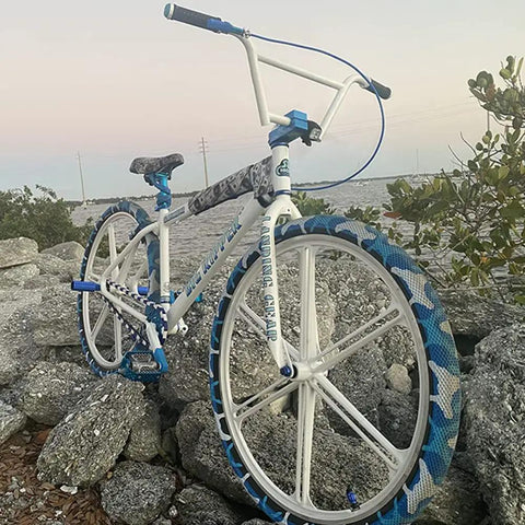 White BMX bike with blue accents on rocky terrain at sunset, showing adjustable 400mm bicycle seat post with tilt head and easy install clamp.