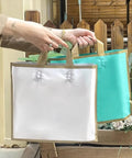 Hands holding two high-end paper gift bags in teal and white, showcasing durable handles and elegant design for weddings or parties.