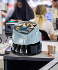 Countertop setup with coin counter and sorter machine with six bins counts up to 250 coins per minute in a busy shop environment.