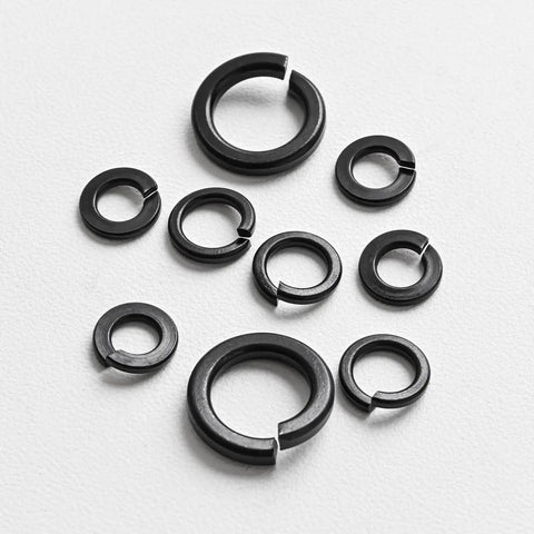 Assorted sizes of Three Eighths Inch Split Lock Washer Set, 50 Pack, Black Oxide 304 Stainless Steel Spring Lock Washers on white surface.