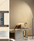 Arc Corner Floor Lamp With 3000K Warm White Cozy Vibes Mood Lighting, Three Brightness Presets, Easy Tap Touch Switch, 63 Inch Curved LED Standing Lamp For Living Room And Bedroom, Sleek Silver Finish next to modern chair and table.