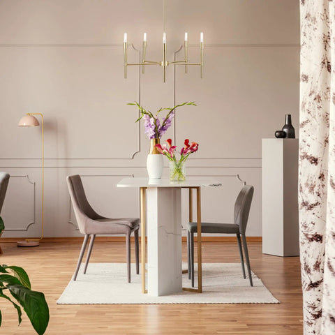 Modern dining room with marble table, gray chairs, floral arrangement, and chandelier lighting.