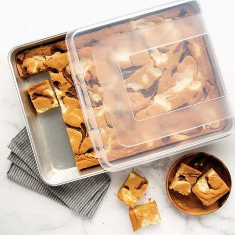 Natural Aluminum High Sided Sheet Cake Pan For Even Browning And Big Batches with brownies and storage lid on marble surface.