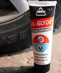 SIL Glyde Brake Lubricant High Temp Formula 8 Oz Tube in front of car tire, showcased for heat resistance and rust protection.