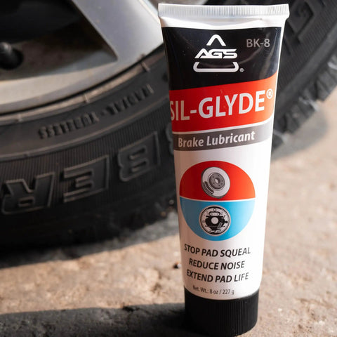 SIL Glyde Brake Lubricant High Temp Formula 8 Oz Tube in front of car tire, showcased for heat resistance and rust protection.