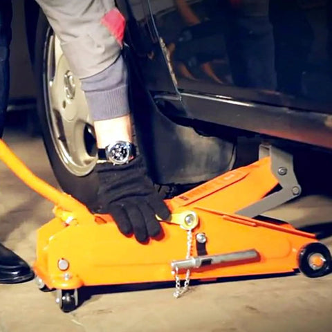 Orange hydraulic floor jack lifting a car; gloved hand near wheel and pinch-weld pad