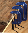 Three sizes of blue woodworking G clamps with quick release C clamp for desk mounting, secured on wooden tabletop.
