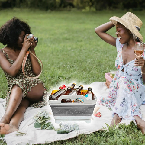 Women enjoying a picnic with a gray Collapsible Wash Basin With Drain Plug 2.4 Gallon Foldable Kitchen Sink filled with drinks.