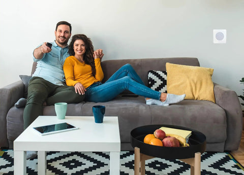 Couple sitting on sofa with Wireless Door Chime With Bright Flashing Strobe Light For Hearing Impaired mounted on wall.