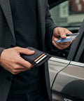 Man holding Ultra Slim Front Pocket RFID Blocking Leather Wallet For Men And Women In Carbon Fiber Black by a car, inserting card.