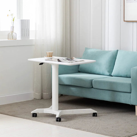 Slick Mobile Lectern Podium Stand With Smooth Roll Sit Stand Laptop Desk And Roomy Notebook Cart Build For Home Office Flex Workstations In Clean White Finish next to a couch.