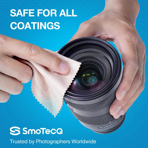 Close-up of hands cleaning a camera lens with a beige SmoTecQ microfiber cloth; blue background.