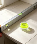 5Pcs Small Circular Bubble Levels with Double Sided Adhesive next to a standard level on tiled surface.