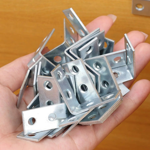 Hand holding 10 Pack Right Angle Corner Brackets For Furniture And Cabinets, Iron Joint Fasteners, 3 x 3 x 1.5 cm, silver finish.