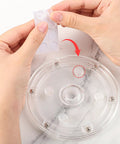 Hands applying rubber feet to the clear acrylic turntable from the Level Up Your Sweet Baking Game With This Solid Acrylic Cookie Decorating Turntable Kit That Comes Loaded With Scribe Needles Soft Brushes Grip Mats And Rubber Feet For Flawless Icing Every Time.