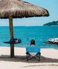 Woman sitting in a blue Low Beach Chair for Beach Tent and Camping, Ultralight Folding Recliner With Cup Holder facing the sea