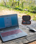 Laptop on wooden table beside open Hard Case For SanDisk Extreme Portable SSD Built Tough Rugged Foam Padding And Mesh Pocket.
