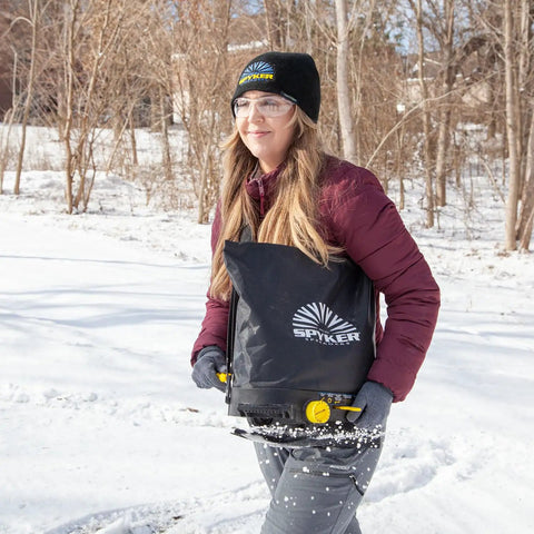 Person using Spyker 25Lb Bag Spreader With Material Viewing Window And Easy Calibration System in snowy landscape
