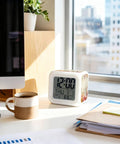 Chill Autumn Floral Silent Alarm Clock With Smooth Snooze And Soft Glowing Nightlight Hella Compact Desk Time Date And Temp Display For Bedrooms And Home Offices beside a coffee cup.
