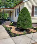 Manicured front yard with gravel beds and neatly trimmed shrubs outside a cream-colored house with brown shutters.