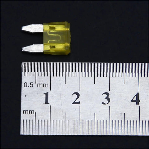 Close-up of a yellow blade fuse next to a ruler for size reference, part of the 600Pcs Auto Fuse Kit With Blade Fuses 5A 10A 15A 20A 25A 30A For Cars And Trucks, Easy Replace With Fuse Puller, Quick Identification, Must Have Safety Backup For DIY Electrical Repairs On The Go.