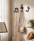 Fresh Black Cast Iron Musical Note Wall Hooks Set Of Three Decorative Coat Rack With Mounting Screws Hanging Clothes Bags And Keys In Music Room Or Kitchen Vibe on a wall, holding a bag.