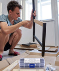 Person assembling furniture with 720 Pcs M3 Hex Socket Cap Bolts Screws Assortment Kit in foreground, DIY project setting