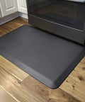 Anti Fatigue Floor Mat With Cushioned PU Comfy For Home Kitchen Garage And Office Standing Desks Water Resistant Ergonomic Pad placed in front of a kitchen oven on wooden flooring.