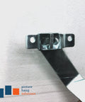 Close-up of 100 Pack T-Screw Security Hanging Kit With Wrench For Art And Frames on a wall, metal bracket in focus.