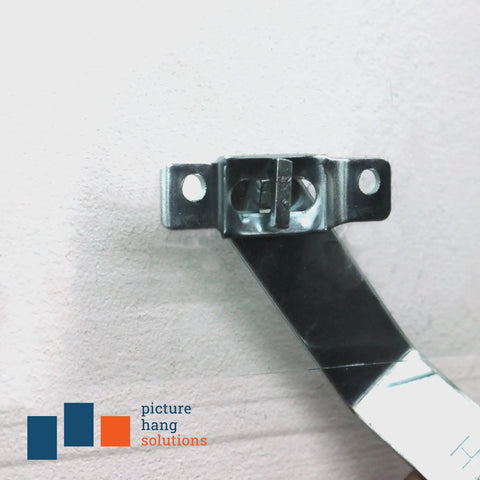 Close-up of 100 Pack T-Screw Security Hanging Kit With Wrench For Art And Frames on a wall, metal bracket in focus.