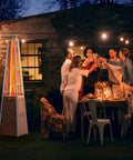 IDEASURE patio propane heater tower with white finish, glowing flame at outdoor dinner party scene