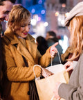 Smiling woman receives brown paper bag with handles during festive night event outdoors.