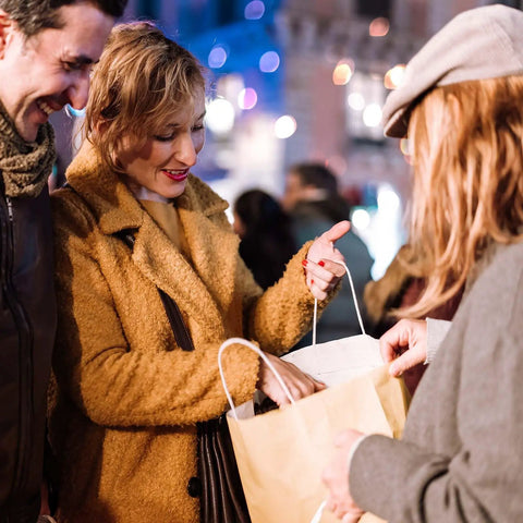 Smiling woman receives brown paper bag with handles during festive night event outdoors.