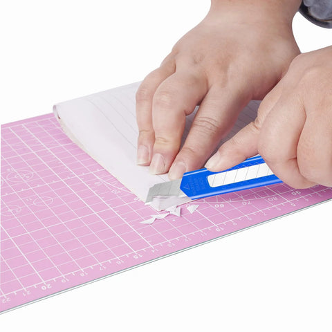 Blue retractable utility knife cutting white paper on pink cutting mat.