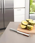 V Shape Pineapple Eye Remover Tool With Multipurpose Clip Stainless Steel Peeler next to sliced pineapples on kitchen counter