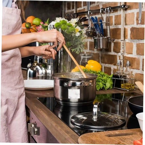 Person in apron stirring pot on stove in kitchen with utensils and fresh vegetables around