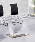 Modern dining table with marble pattern top, surrounded by black chairs, in a bright room with large window and stone wall.