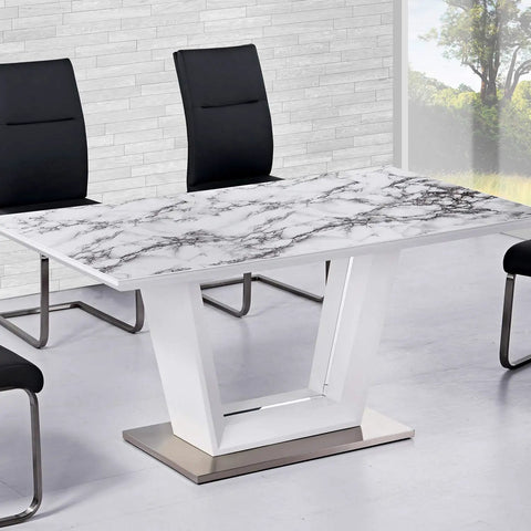 Modern dining table with marble pattern top, surrounded by black chairs, in a bright room with large window and stone wall.