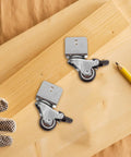 Rugged Swivel Furniture Casters With Gliding Silent Rollers And Tough Round Plates fastened to a wooden board with gloves and pencil.
