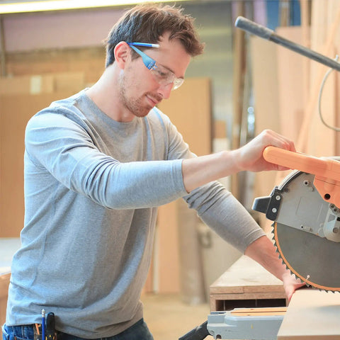Man wearing 48 Pack Safety Glasses With Clear Lenses For Work And Lab Eye Protection Goggles using saw, blue frame visible