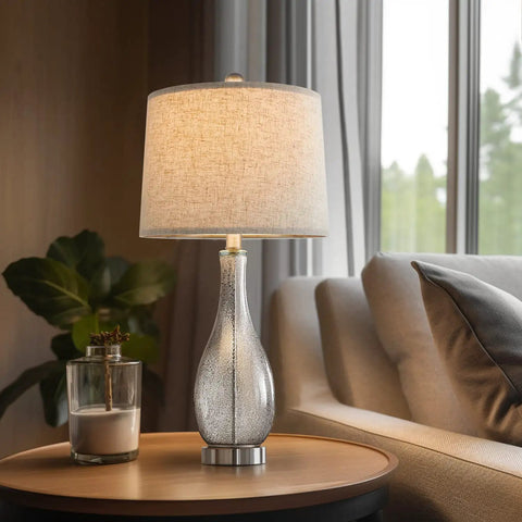 24.5 Inch Glass Table Lamps Set Of 2 With USB Charging Ports, Nightstand Bedside Lamps For Living Room Bedroom Office Or College, Modern Silver Finish, Built In 5V/2A USB Ports That Charge Your Phone On Or Off on a wooden table by a sofa.