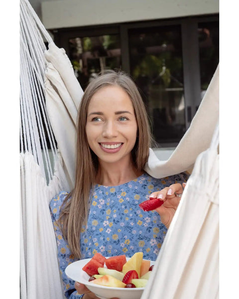 Woman enjoying fruit in Heavy Duty Hammock Chair With Two Cushions And Protective Waterproof Cover For Indoor And Outdoor Relaxation.