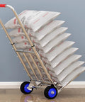 Hella Tough Folding Sack Truck With Solid Rubber Wheels And Rugged Utility Dolly Platform For Zero Sweat Heavy Moving Gear Hauling Up To Two Hundred Forty Two Pounds, loaded with stacked bags.