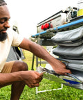 Person using Hanging Organizer For Outdoor FlexRail Camp And Cook Table, Durable Weather Resistant Pocketed Storage attached to four foot system