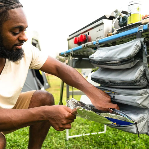 Person using Hanging Organizer For Outdoor FlexRail Camp And Cook Table, Durable Weather Resistant Pocketed Storage attached to four foot system